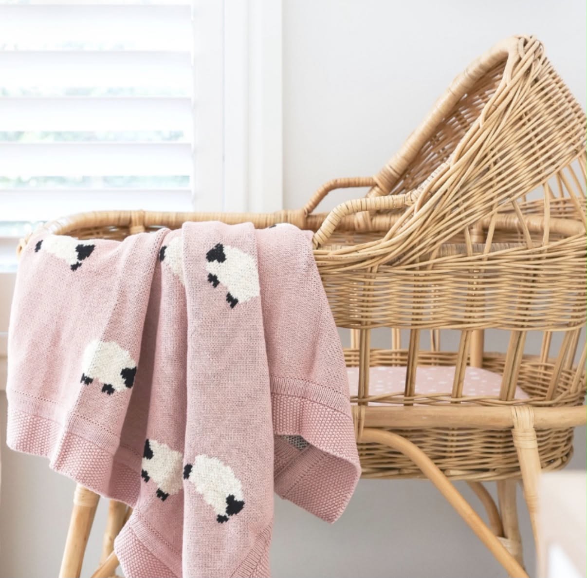 Pink knitted sheep blanket draped over a rattan bassinet